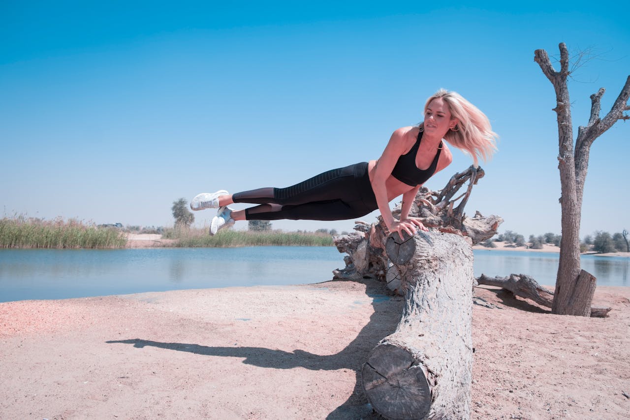 Woman Jump on Tree Log Near Body of Water Under Blue Sky